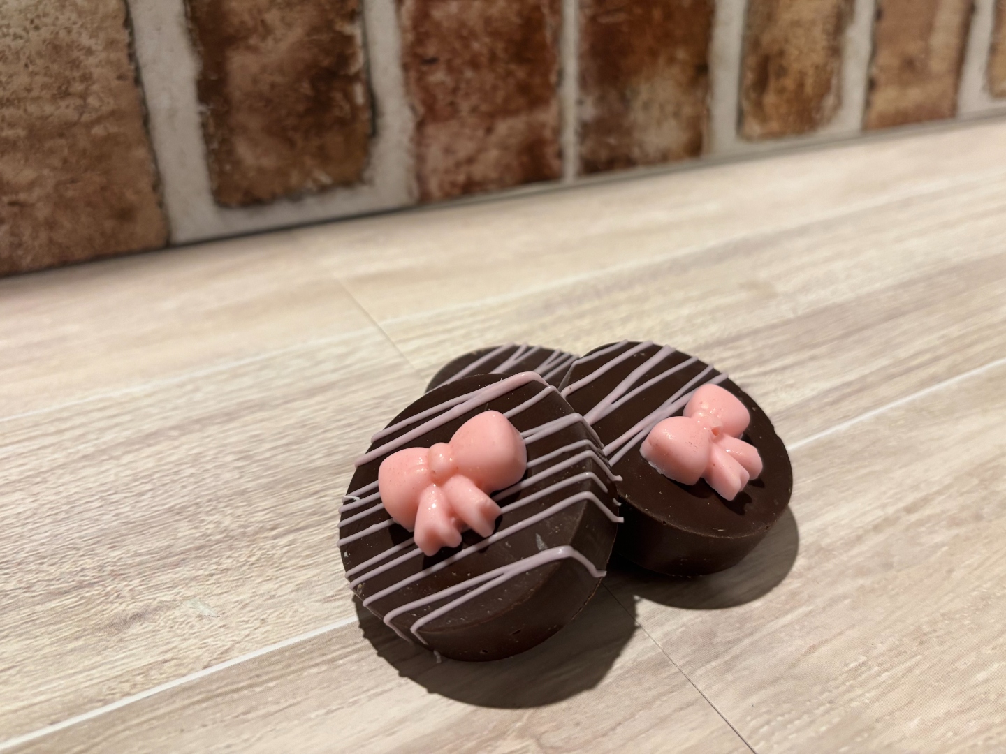 Chocolate covered Oreos with pink bow accents on a wood surface